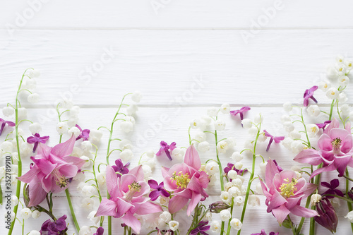 Flowers flat design. Floral composition with pink and purple Aquilegia and Convallaria flowers. Template with copy space on white wooden board