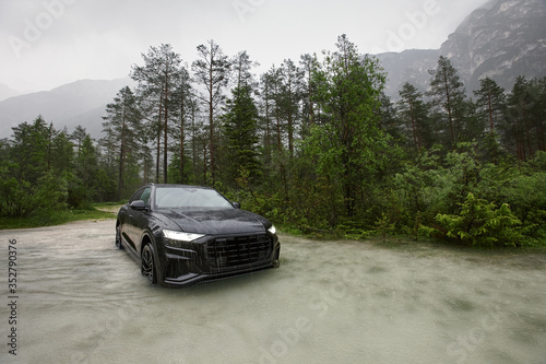 Sporty black crossover car in water in rain on mountains background