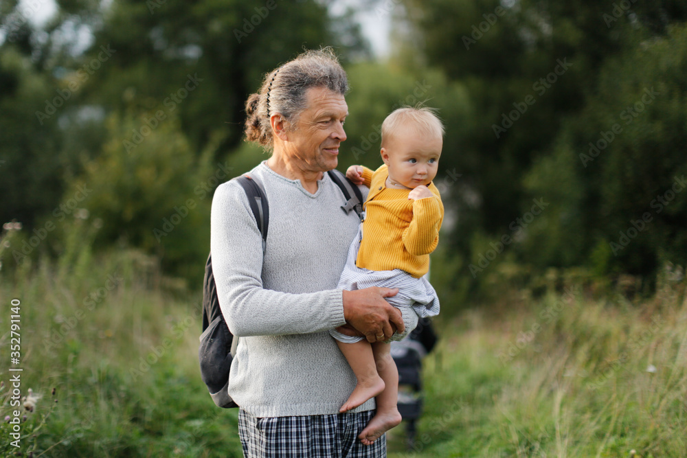 Caucasian dad with baby walks in deserted places near house, father holds one-year-old baby in his arms, walking in park, concept of fatherhood and summer, social distance from other people