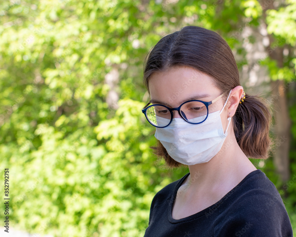 Close-up portrait of a beautiful young woman wearing a disposable medical face mask in the park. Safety in a public place with the Covid-19 epidemic. Copy space Close-up portrait of a beautiful young woman wearing a disposable medical face mask in the park. Safety in a public place with the Covid-19 epidemic. Copy space