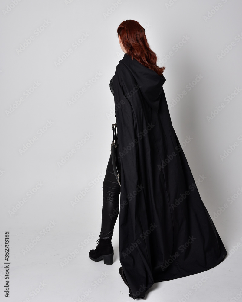 fantasy portrait of a woman wearing long black cloak. Full length standing pose with back to the camera, isolated against a studio background. fantasy portrait of a woman wearing long black cloak. Full length standing pose with back to the camera, isolated against a studio background.