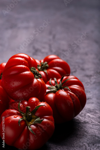 in the foreground, on a textured black background, some ripe and fresh tomatoes covered with drops of water. Copy space