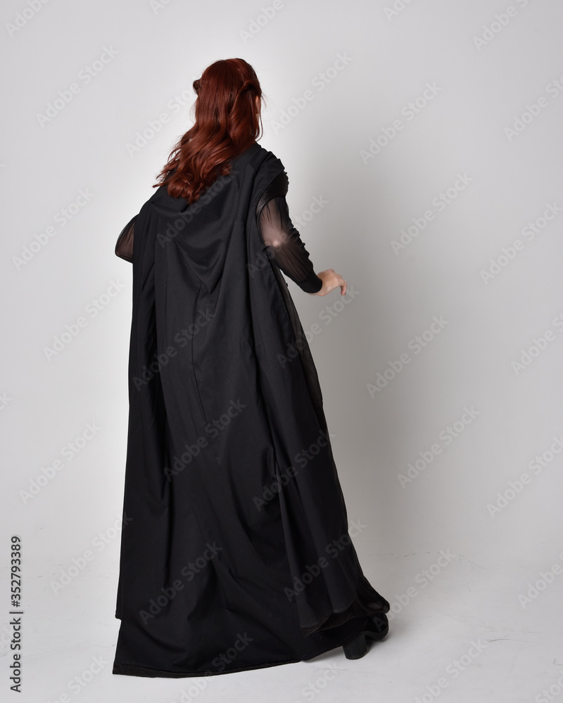 fantasy portrait of a woman wearing long black cloak. Full length standing pose with back to the camera, isolated against a studio background. fantasy portrait of a woman wearing long black cloak. Full length standing pose with back to the camera, isolated against a studio background.
