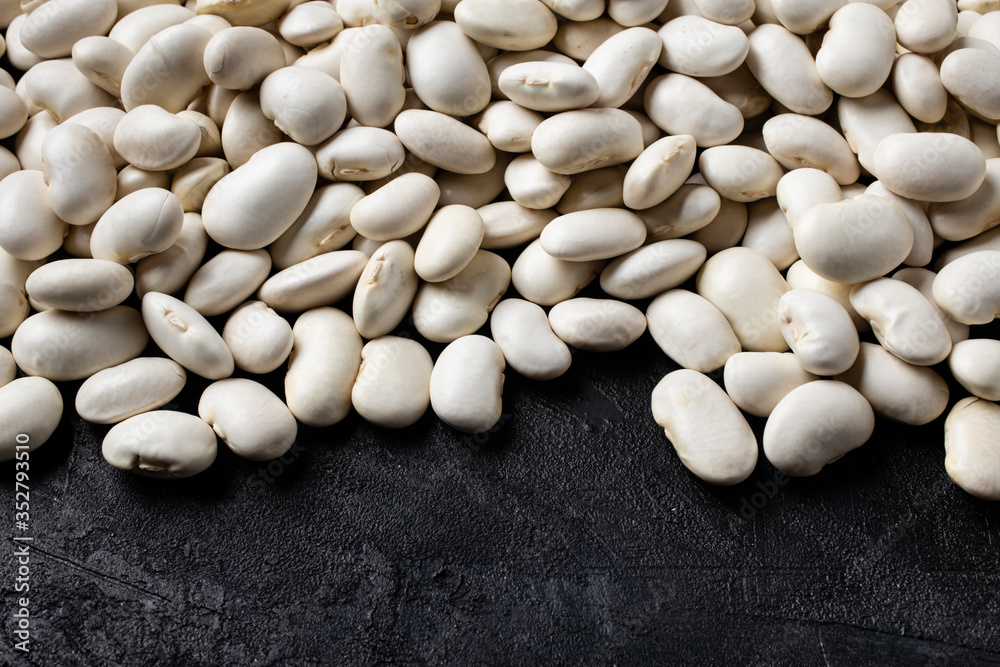 on a textured black background, in the foreground, a pile of dry and raw white beans rich in protein.