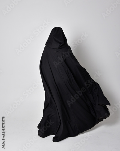 fantasy portrait of a woman wearing long black cloak. Full length standing pose  with back to the camera, isolated against a studio background. photo