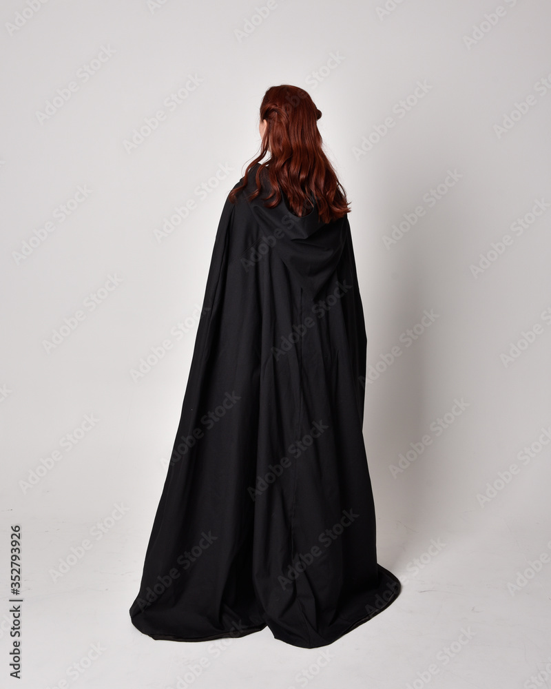 fantasy portrait of a woman wearing long black cloak. Full length standing pose with back to the camera, isolated against a studio background. fantasy portrait of a woman wearing long black cloak. Full length standing pose with back to the camera, isolated against a studio background.