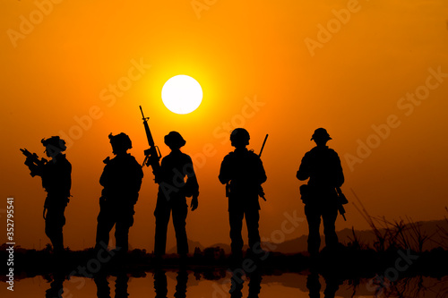 The military silhouettes of soldiers hold gun against with sunset sky background. © APchanel