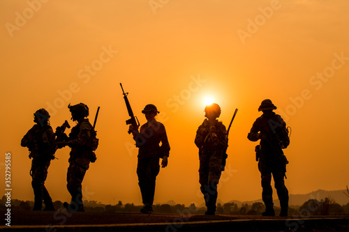 The military silhouettes of soldiers hold gun against with sunset sky background.