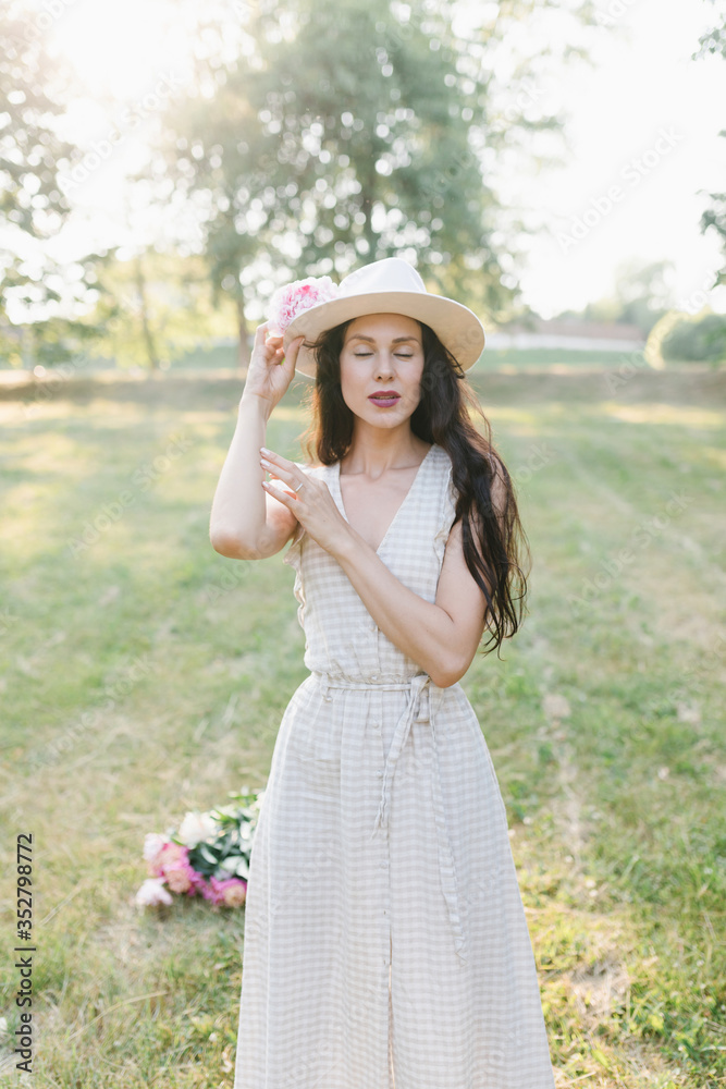 Portrait of a young woman in a hat. Beautiful stylish girl in a summer dress, a hat and a flower in her hand.