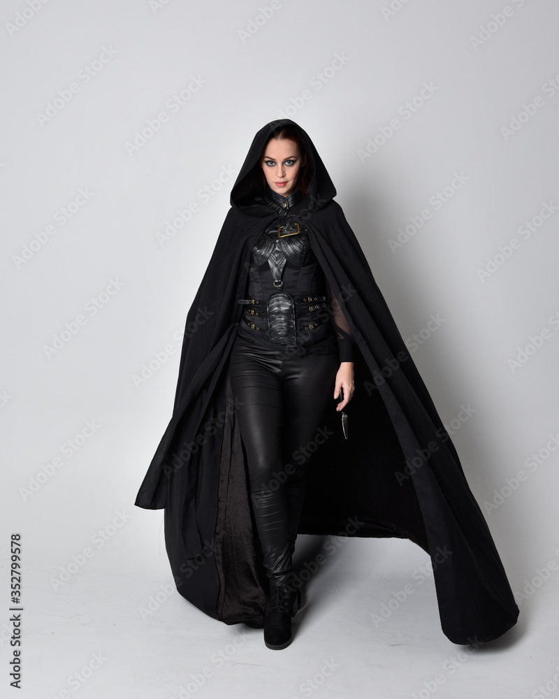 fantasy portrait of a woman with red hair wearing dark leather assassin  costume with long black cloak. Full length standing pose isolated against a  studio background. Stock Photo | Adobe Stock
