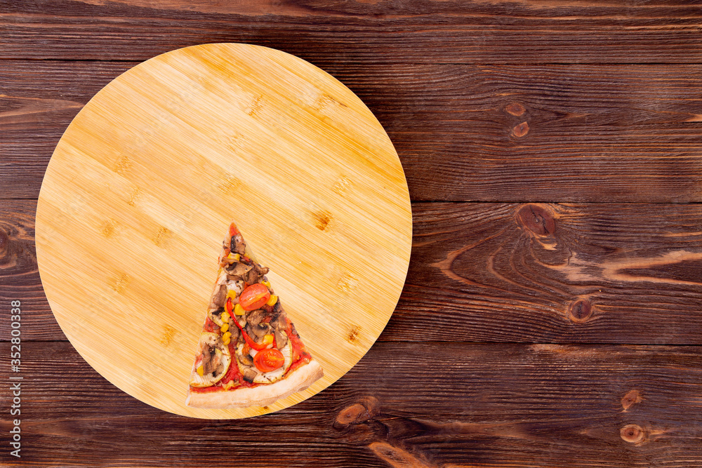 A slice of tasty pizza with mushrooms, corn, cherry tomatos, courgettes and bell peppers on a round platter which is on wooden brown background, top view and copy space A slice of tasty pizza with mushrooms, corn, cherry tomatos, courgettes and bell peppers on a round platter which is on wooden brown background, top view and copy space