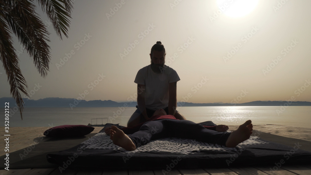Silhouette of masseur doing thai yoga massage for a woman at sunrise outside.