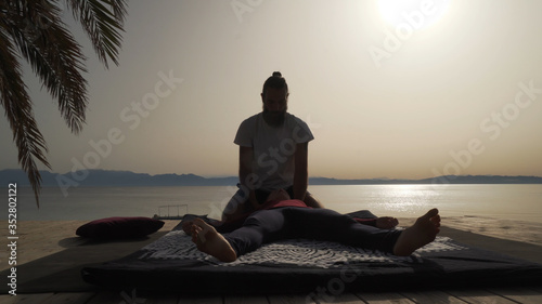Silhouette of masseur doing thai yoga massage for a woman at sunrise outside.