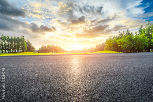 Asphalt road and green grass with forest landscape at sunset.