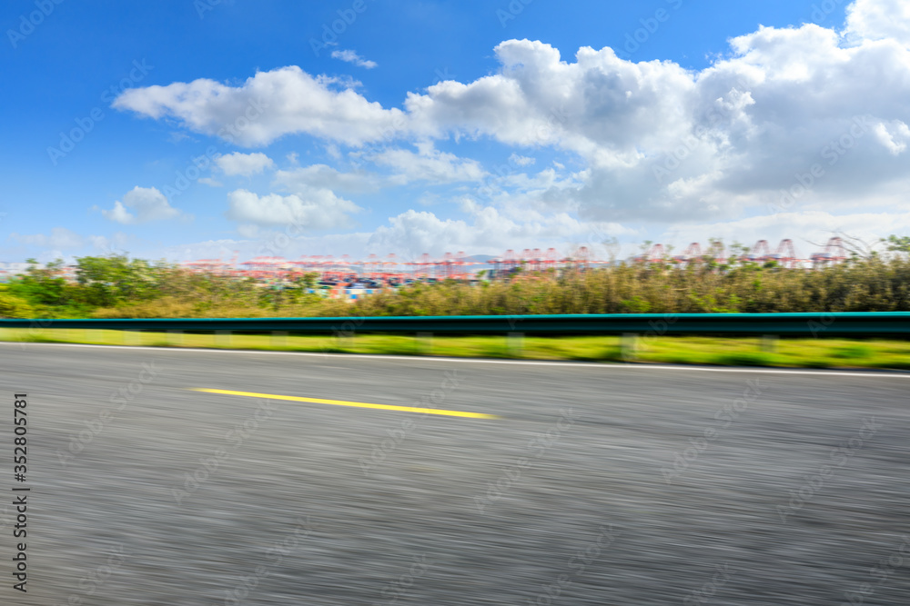 Motion blurred asphalt road and container port terminal landscape under blue sky.