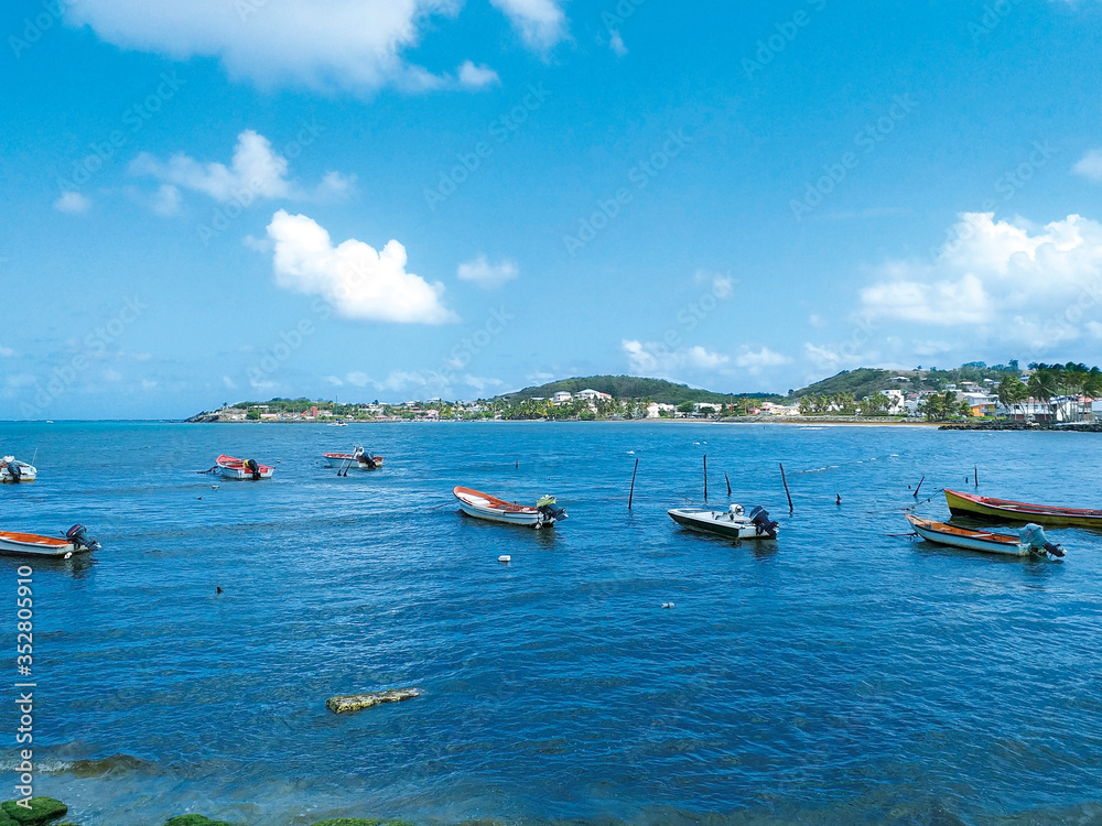 Turquoise waters of the Caribbean Sea with traditional fishing boats and the silhouette of a small town in the background. Idyllic tropical landscape. Authentic Caribbean spot.