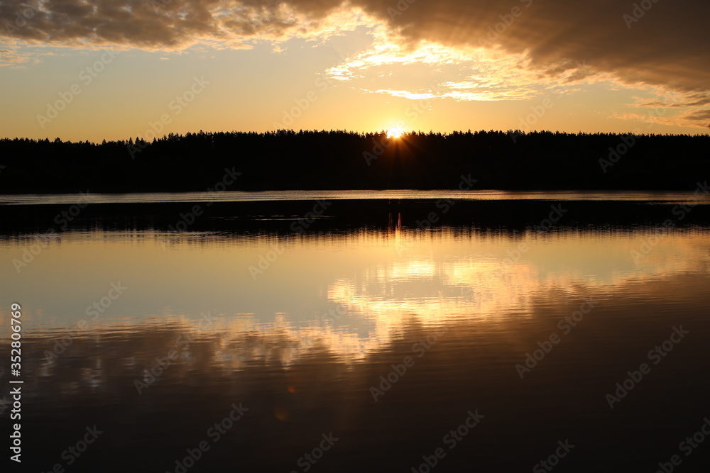 An unusual dawn on the river.Mirror image of the colorful sky in the calm water.The Golden sun beams through the silhouette of the forest illuminating the bronze clouds.Nature is a great artist.Russia