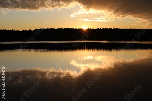 An unusual dawn on the river.Mirror image of the colorful sky in the calm water.The Golden sun beams through the silhouette of the forest illuminating the bronze clouds.Nature is a great artist.Russia