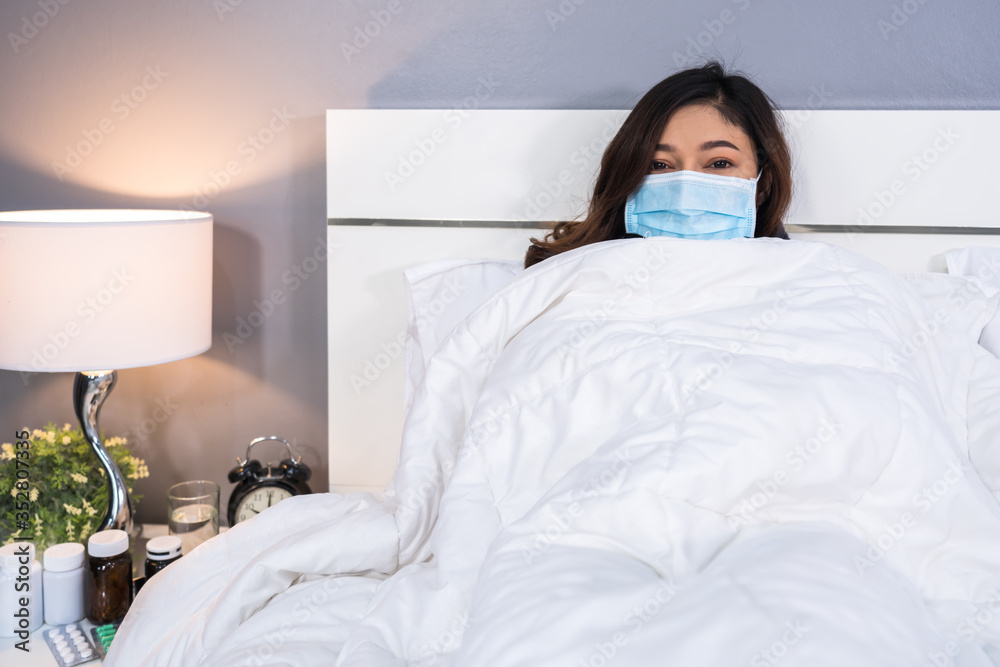 sick woman in medical mask feeling cold and suffering from virus disease and fever in bed, coronavirus (covid-19) pandemic concept.