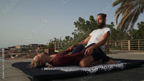 Handsome bearded man doing thai yoga massage for a woman at sunset seashore.