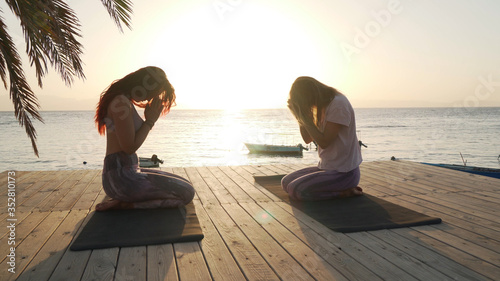Silhouette of two women meditating at seaside at sunset