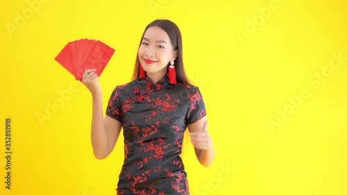 Asian woman in Chinese traditional costume dress showing red envelopes and giving big thumb up a sign on studio yellow background photo