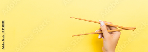 Wooden chopsticks holded with female hands on yellow background. Ready for eating concepts with empty space
