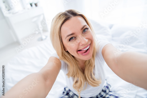 Closeup photo of pretty funny blond lady bedroom making selfies stick tongue out mouth good morning weekend popular blogger influencer freelancer quarantine wear pajama room indoors