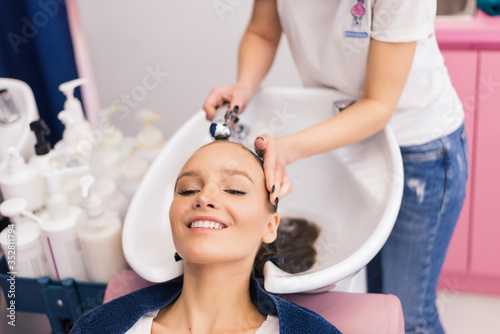 Young pretty woman washing hair before getting new hairstyle at professional hair styling saloon.