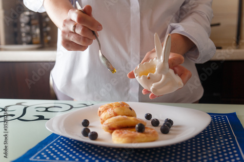 Female hands spkinkling honey on traditional syrniki or cottage cheese pankaces with blueberries and honey on white plate with blue napkin on kitchen table. Healthy breakfast, diet concept. photo