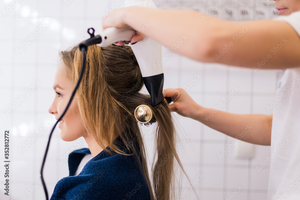 Fototapeta premium Professional woman hairdresser drying woman's hair styling using blow dryer at the hairdressing saloon