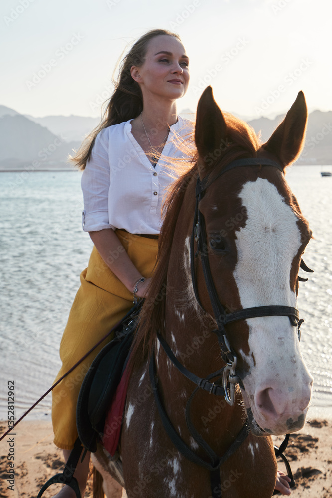 Obraz premium View of young girl sits on a horse in nature at sunset