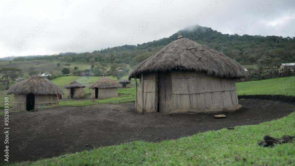 Parallax shot of a straw bamboo hut of the Maasai Massai tribe cultural African village in grassy muddy valley in the mountains of Tanzania on a cloudy day Parallax shot of a straw bamboo hut of the Maasai Massai tribe cultural African village in grassy muddy valley in the mountains of Tanzania on a cloudy day