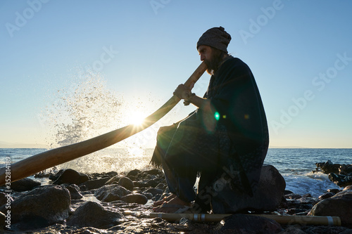 Man playing on Austaralian didjireedoo insturment in sunshine at seashore