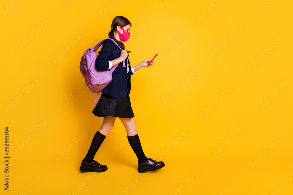 Full body profile side photo high school student girl go walk lesson use smartphone wear black blazer jacket skirt long socks backpack medical mask isolated yellow color background