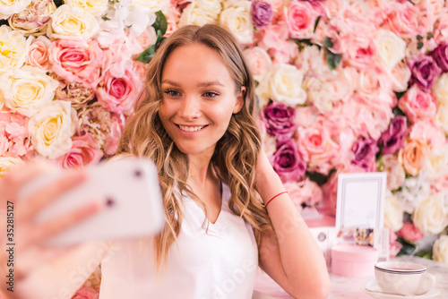 Young curly woman taking a selfie at the cafe on flowers background