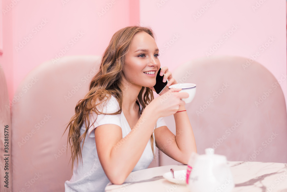 Young happy woman talking on mobile phone with friend while sitting alone in modern coffee shop.