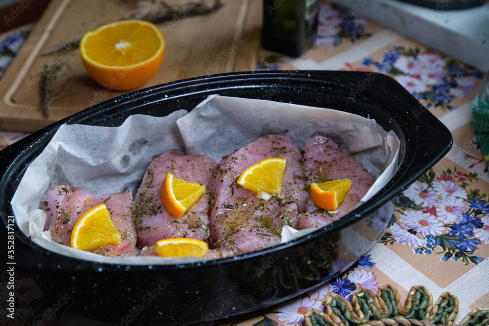Raw chicken (turkey) fillet covered with herbs and orange slices in oven tray prepared for roasting. Homemade cooking.