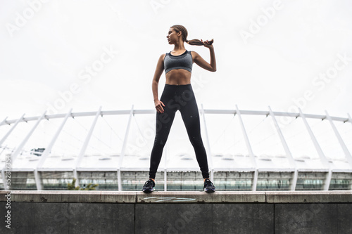 Beautiful strong and sporty young woman in sportswear stands in confident pose on the rooftop. Outdoors workout concept