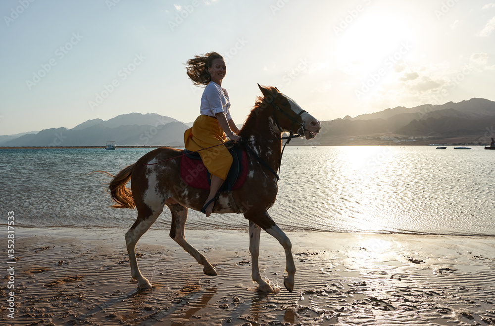 Caucasian blonde girl riding horse at sunset beach Caucasian blonde girl riding horse at sunset beach