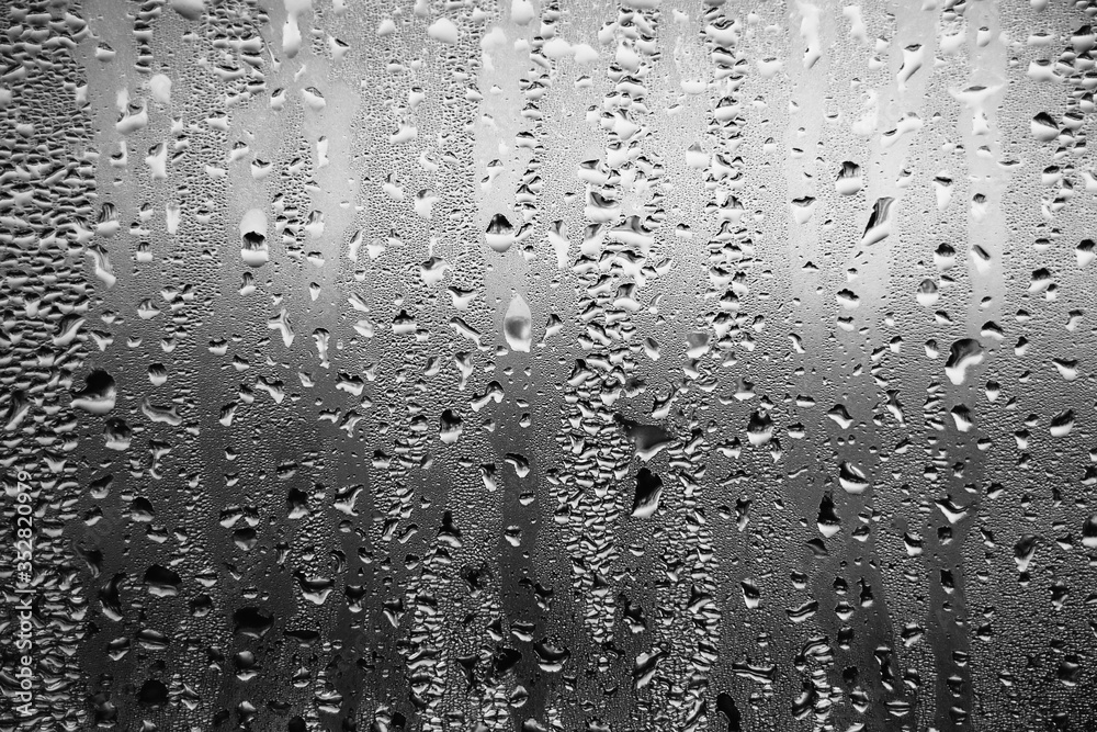 Fototapeta premium Black and white background depicting raindrops running down the glass on the window in a dark sad cloudy weather. Melancholy.