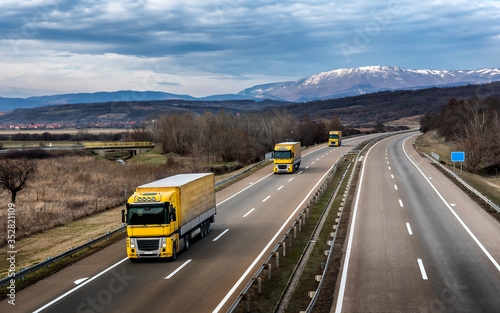 Fleet of Yellow Trucks in line as a convoy at a rural countryside highway under a beautiful blue sky