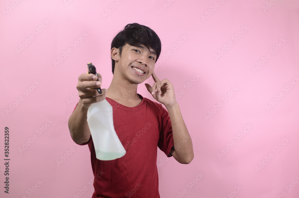 Man with water sprayer in hand. Asian men wearing red t shirts isolated on a pink background Man with water sprayer in hand. Asian men wearing red t shirts isolated on a pink background