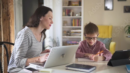 Wallpaper Mural American woman works with laptop remotely and helps schoolboy in learning at table in home spbd. Young mother is working with computer and talking with her son who writing in notebook during online Torontodigital.ca