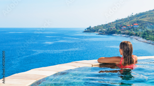 Happy girl have fun on summer beach holiday. Young woman relaxing at edge of infinity swimming pool with sea view from hill top. Healthy family lifestyle, summer travel with kids on tropical islands.