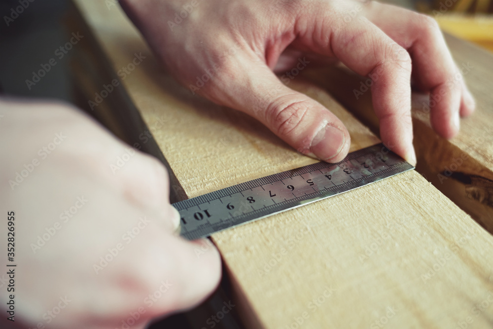 Construction and repair. Men's hands line measure the width of a wooden board. Hands with a close-up tool.