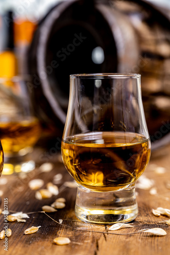 Fototapeta Naklejka Na Ścianę i Meble -  Small tasting glasses with aged Scotch whisky on old dark wooden vintage table with barley grains