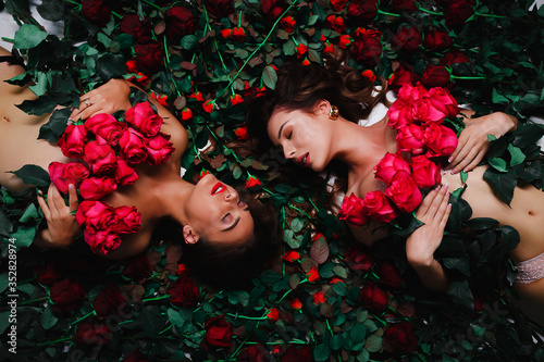 Two brunettes are lying on the flowers, covered with red roses