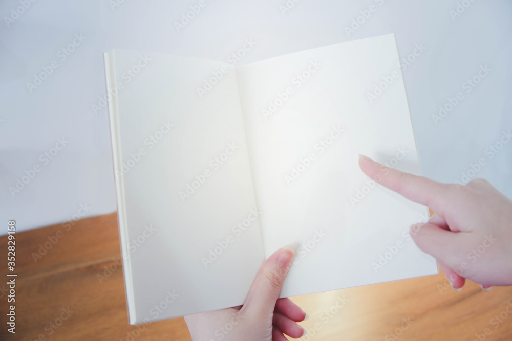 Closed up image of hands opening a notebook. Blank page. Background of a wood desk.