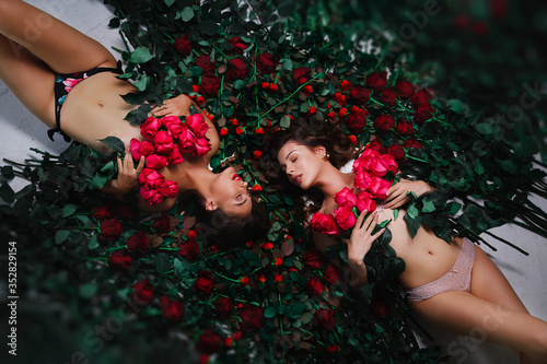 Two brunettes are lying on the flowers, covered with red roses